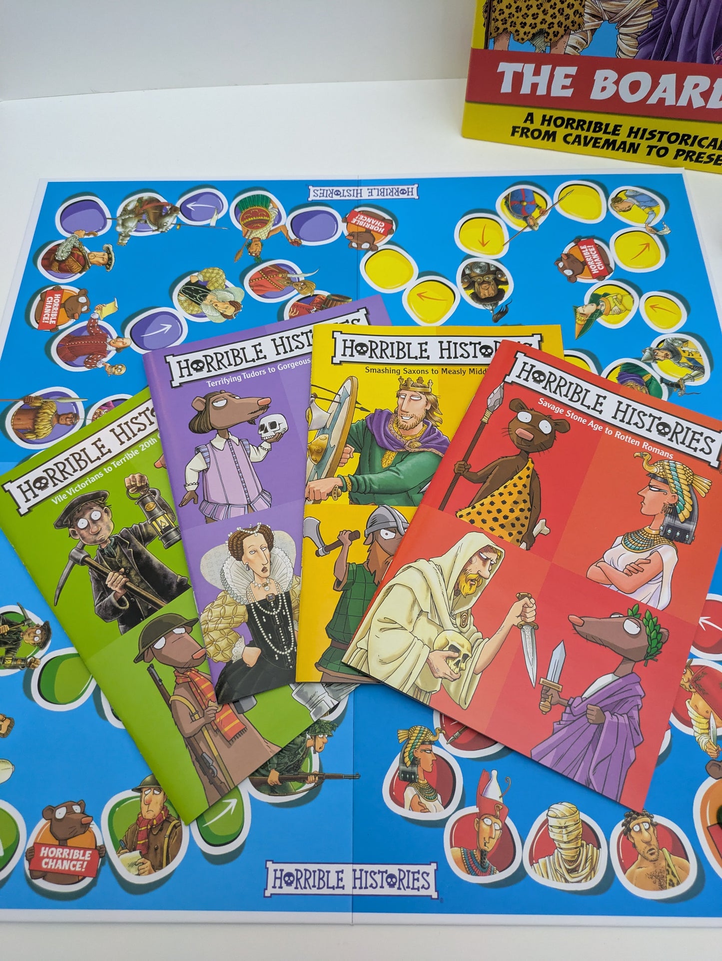 Colour-coded question booklets for Horrible Histories: The Board Game, covering different historical eras like the Awful Ancients and Vile Victorians.