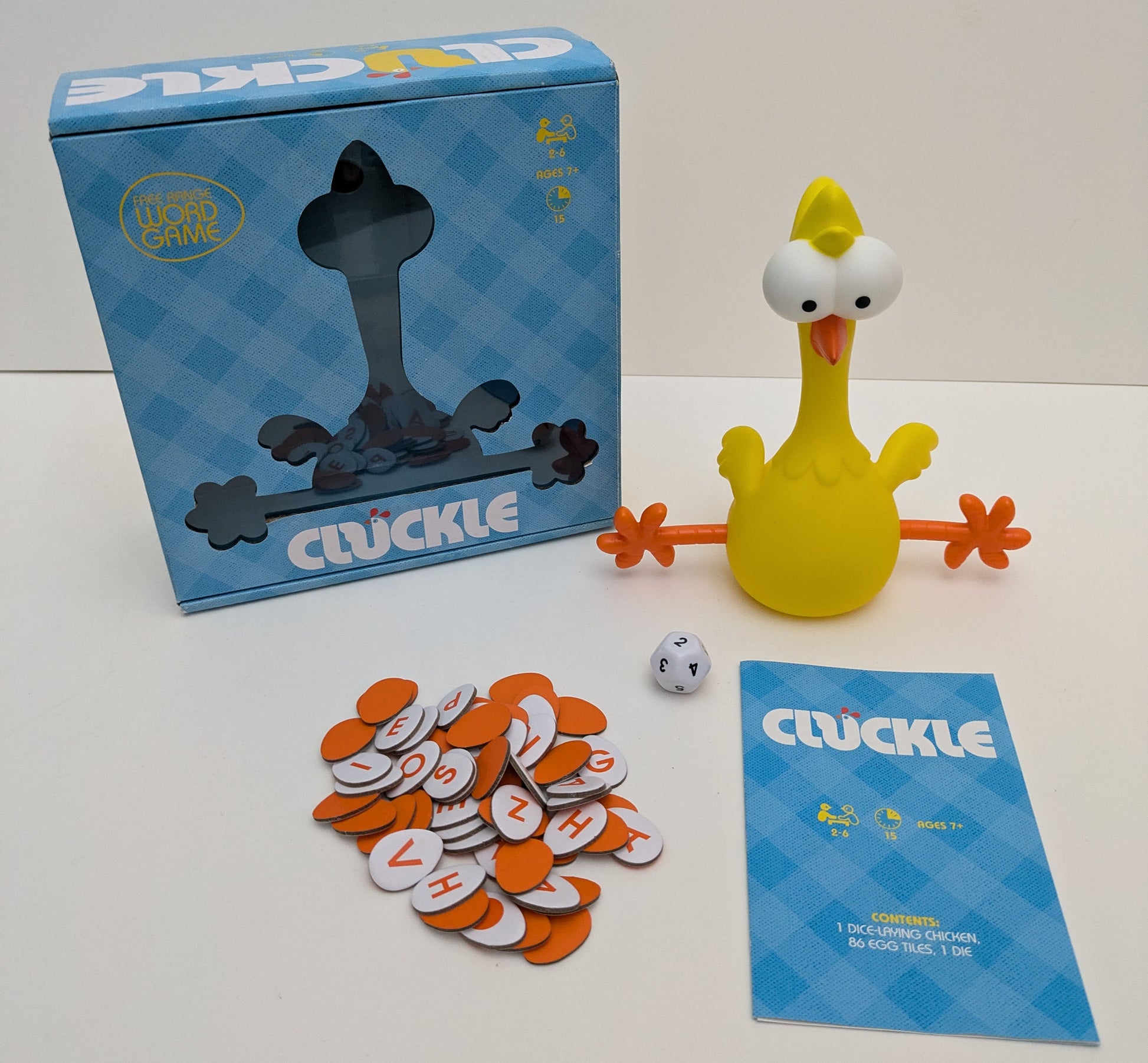 "Complete Cluckle (2021) game setup with egg tiles, rubber chicken, and scoring board ready for a fast-paced word creation race."