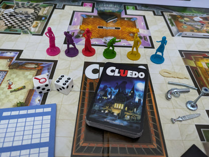 Complete setup of Cluedo (2012) with board, suspect cards, weapon tokens, and player pieces ready for a thrilling mystery game night.