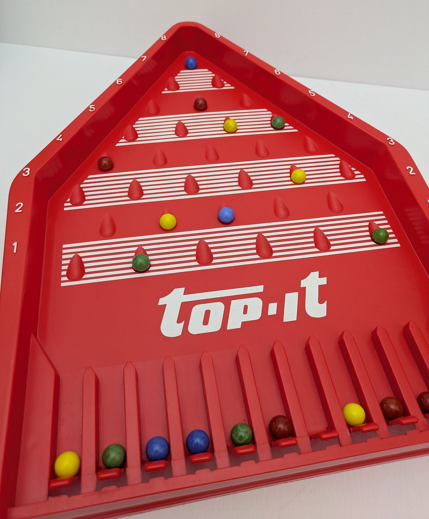 Top-It (1972) is a classic marble skill game where players take turns launching marbles to score the highest points.