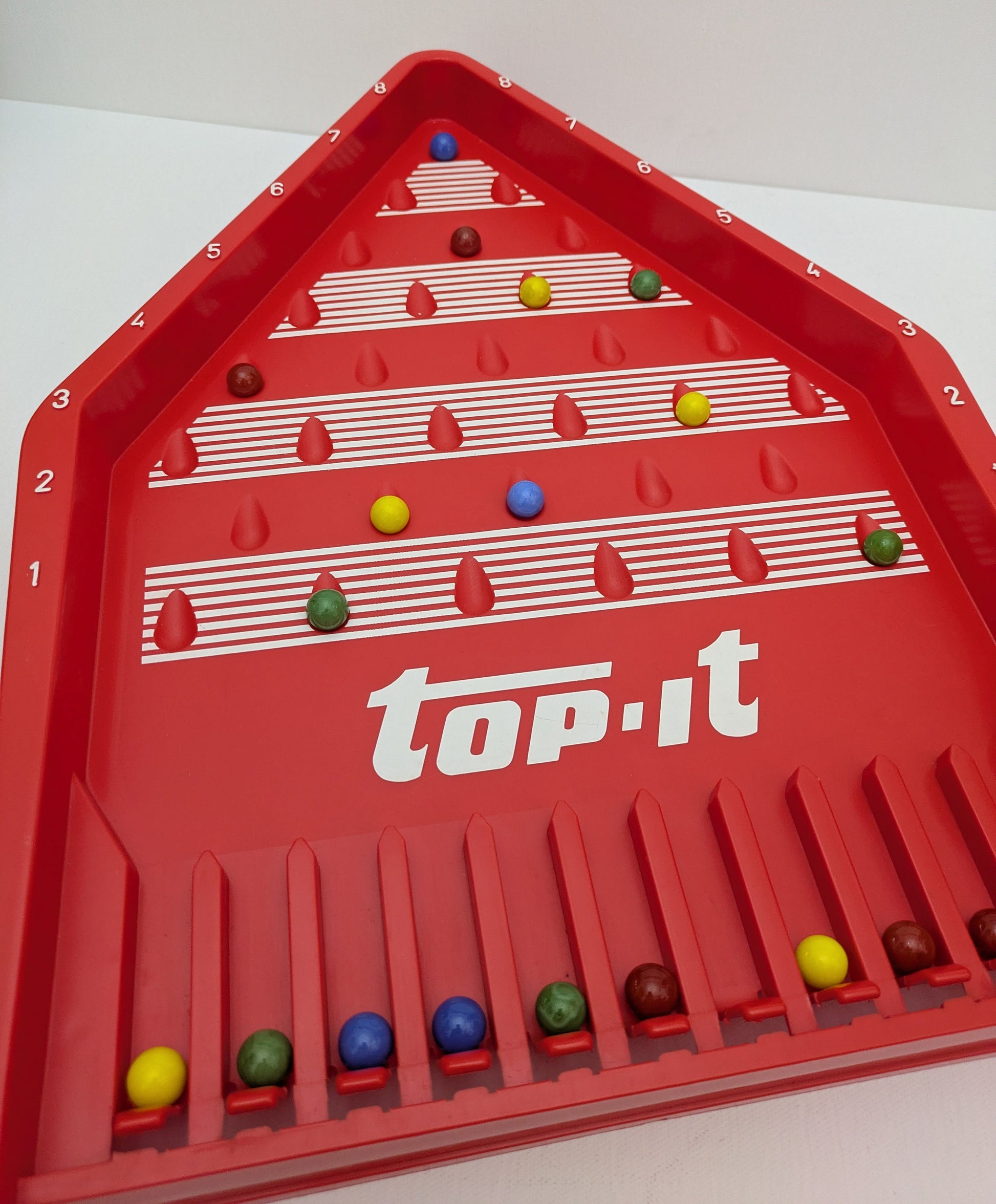 Top-It (1972) is a classic marble skill game where players take turns launching marbles to score the highest points.